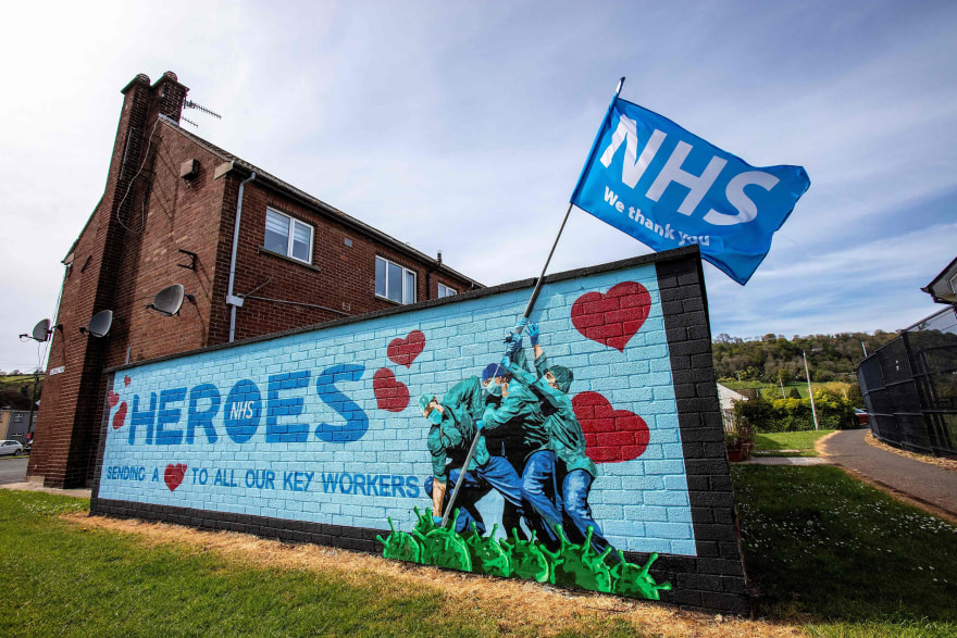 The cover of our 'Voices from the NHS: A People's History' comic book, created by Darryl Cunningham and available to download for free from this blog. A smiling nurse holding a baby stands at the centre of a group of NHS staff and patients representing the diversity of the organisation. Behind them is a landscape including buildings and fields.